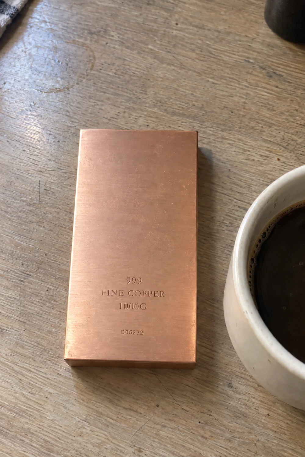 Børstet kobberbarre på et trebord ved siden av en kaffekopp